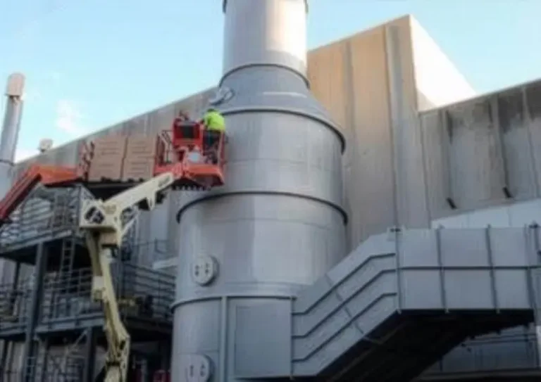 Worker in a lift basket beside a large stainless steel air scrubbing tank