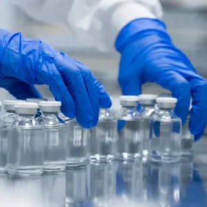 Technician in blue gloves handling glass vials in a chemical laboratory